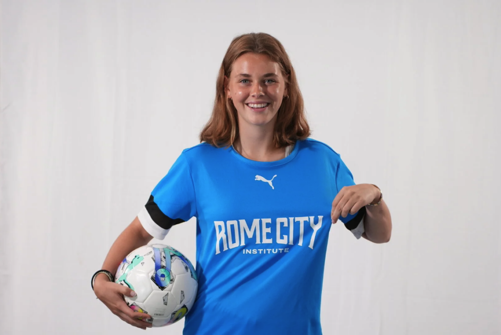 Female player wearing Rome City Institute training kit, holding a soccer ball